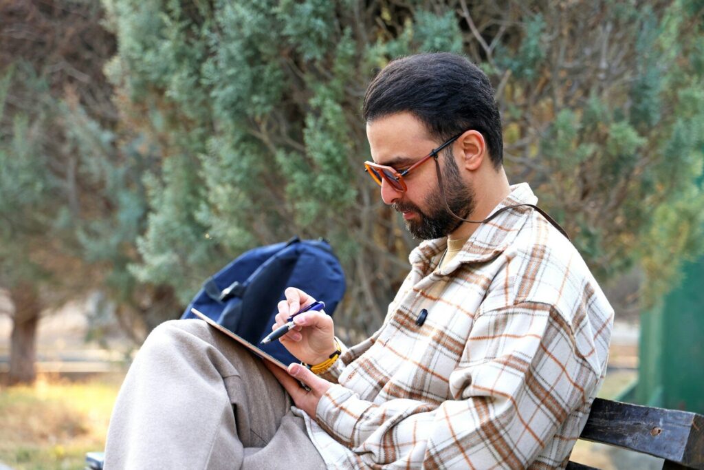 Man sitting on a bench, writing on a tablet.